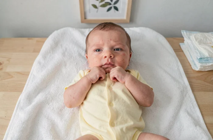 Bébé de 3 semaines allongé sur une table à langer vue du dessus, portant un body jaune pâle, les poings fermés